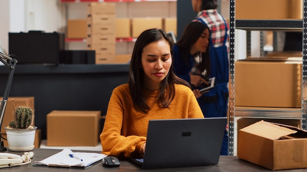 Mulher empresária verificando a produção de estoque no pc, usando o laptop para trabalhar no gerenciamento de pedidos da cadeia de suprimentos. Transporte de planejamento de jovens adultos para o desenvolvimento de pequenas empresas. Tiro portátil.