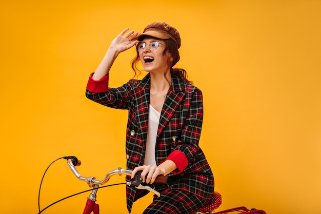 Mulher encantadora com boné da moda e aulas andando de bicicleta na parede laranja