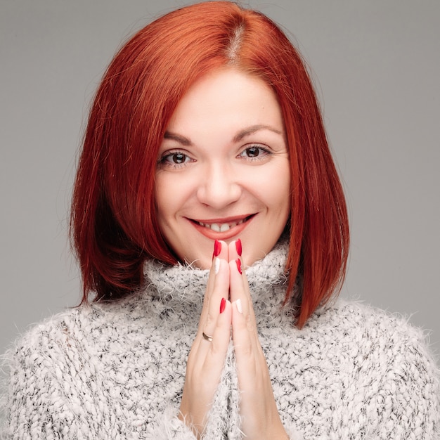 Foto mulher encantadora com cabelo ruivo, sorrindo e juntando as mãos.