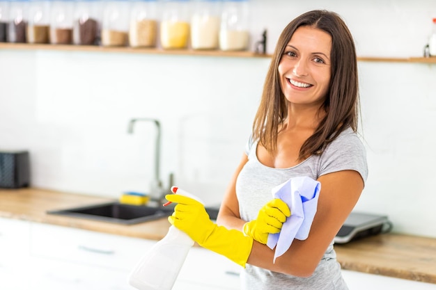 Mulher encantadora com luvas de proteção com spray e pano para limpar a cozinha