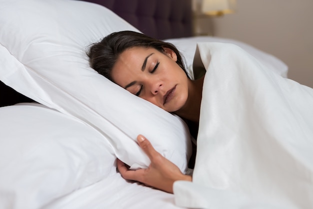 Mulher encantadora dormindo na cama branca