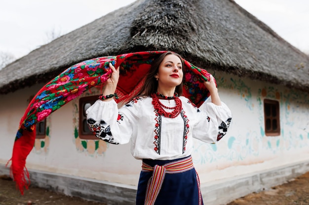 Mulher encantadora no tradicional colar de lenço ucraniano e vestido bordado em pé no fundo da cabana decorada estilo ucraniano cultura étnica folclórica