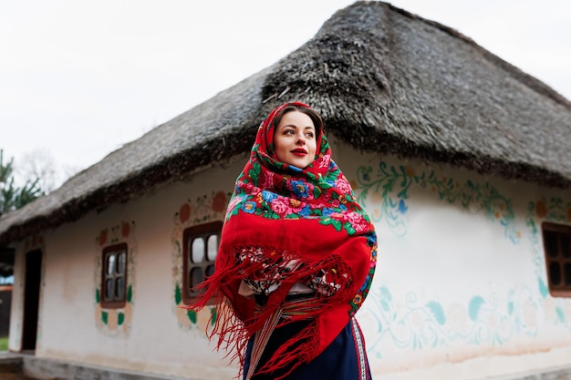 Mulher encantadora no tradicional colar de lenço ucraniano e vestido bordado em pé no fundo da cabana decorada estilo ucraniano cultura étnica folclórica