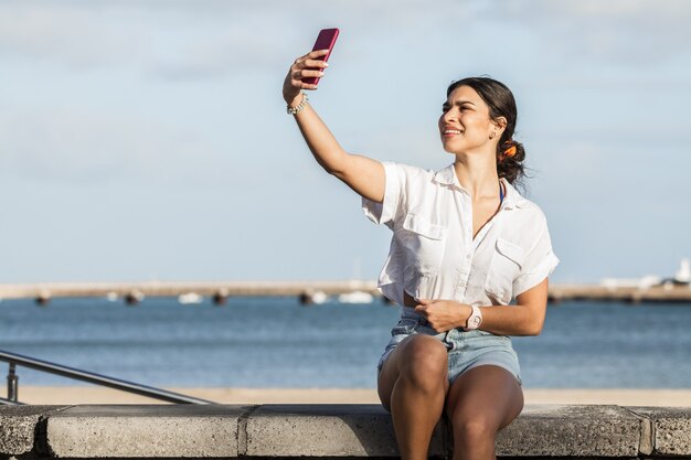 Mulher encantadora tirando selfie em smartphone no aterro