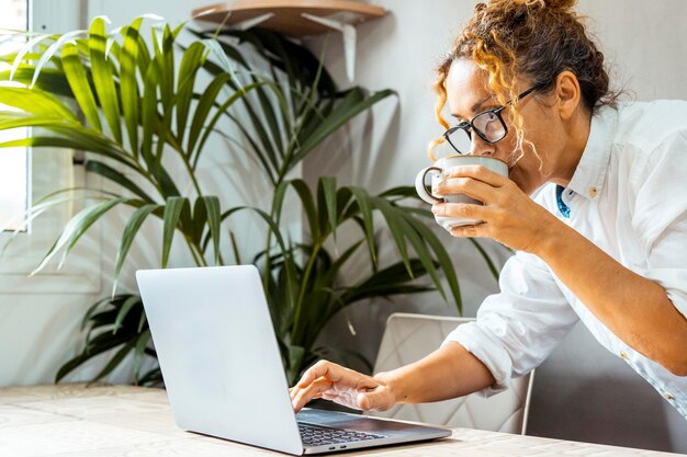 Foto mulher encaracolada com óculos usando laptop comunicando-se na internet com um cliente em casa escritório aconchegante de trabalho conceito de aprendizagem eletrônica de trabalho remoto