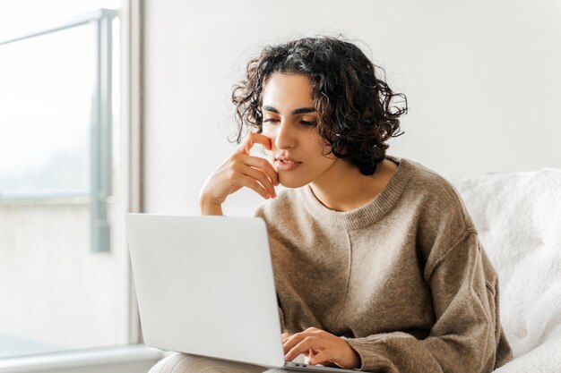 Foto mulher encaracolada focada procurando tela de computador portátil estudando aprendizado de língua estudante sério procurando informações trabalhando on-line sentado em casa conceito de educação