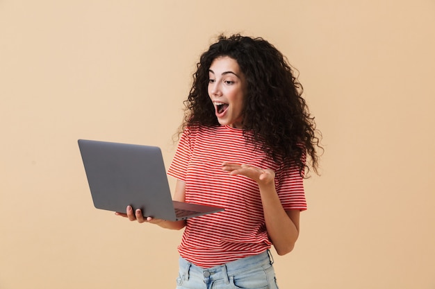 Mulher encaracolada muito jovem incrível usando o computador portátil.