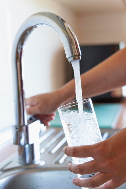 Mulher enchendo um copo de água fria na torneira da cozinha