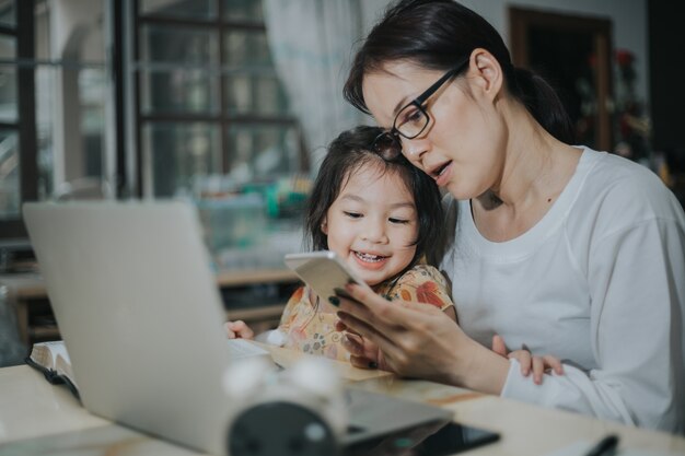 Mulher ensinando a filha com laptop e smartphone estudo online