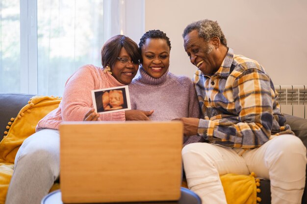 Mulher ensinando o ultrassom de seu futuro filho online com seus pais orgulhosos ao lado de seus avós Concept Maternity Family