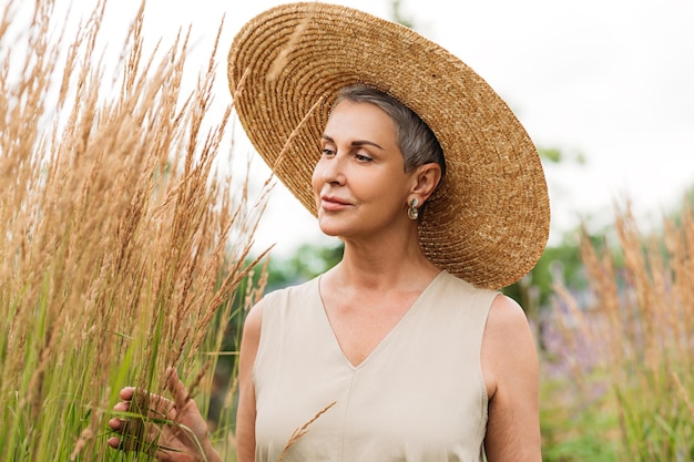 Mulher envelhecida em um chapéu de palha no campo no verão