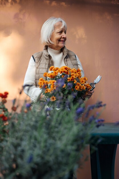 Mulher envelhecida feliz trabalhando com flores desabrochando no jardim.