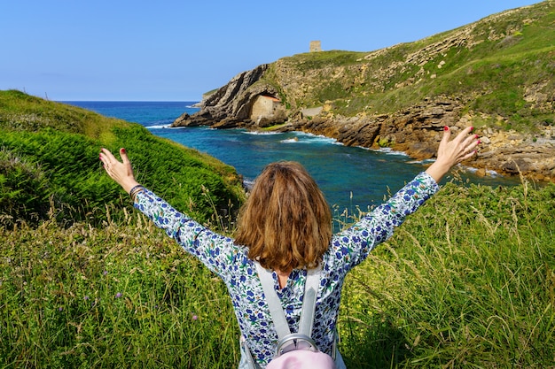 Mulher erguendo os braços de felicidade, olhando para a paisagem marinha