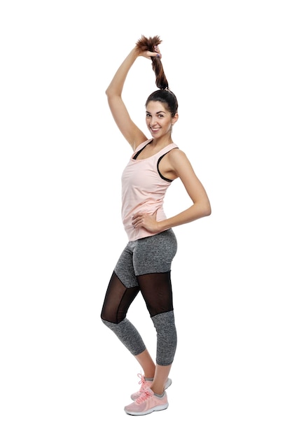 Foto mulher esbelta sorridente em roupas esportivas uma bela morena segura sua trança em leggings pretas e um top rosa atividade energia e esporte isolado em um fundo branco altura completa vertical