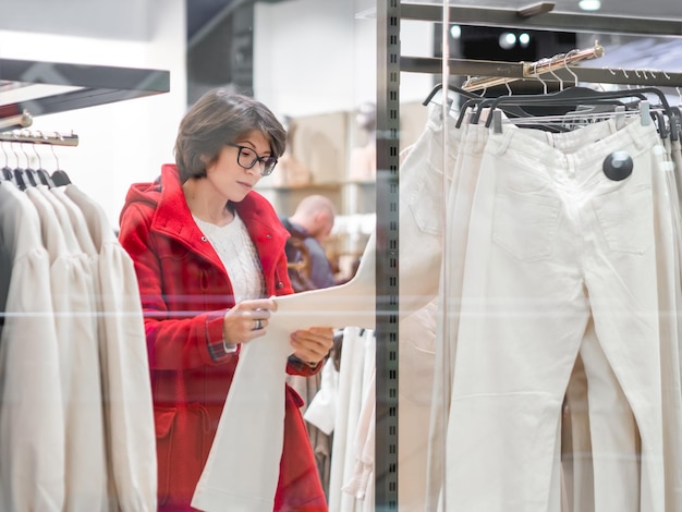 Mulher escolhe calças em loja de roupas calças casuais em ganchos vitrine de loja de compras no centro comercial