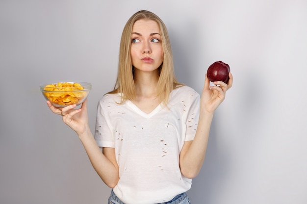 Mulher escolhe entre chips e maçã vermelha em fundo cinza