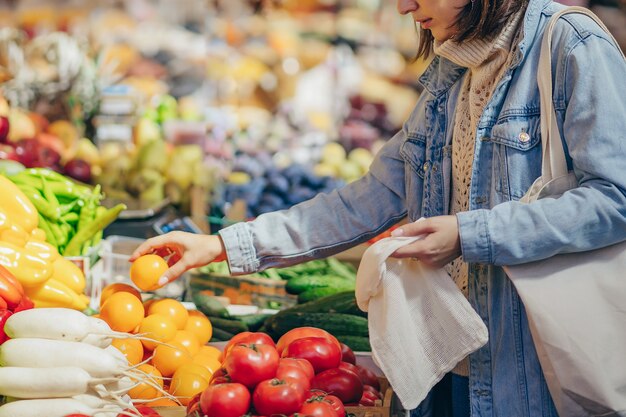 Mulher escolhe frutas e vegetais no mercado de alimentos. Saco ecológico reutilizável para fazer compras. Estilo de vida sustentável. Conceito ecológico.