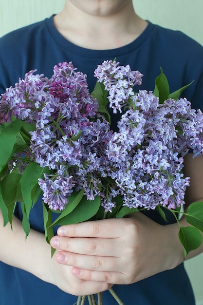 Mulher escondendo a cabeça no buquê de flores lilás sobre fundo azul colorido.