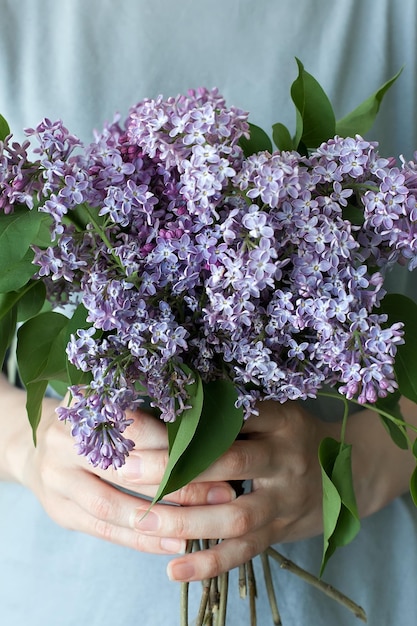 Mulher escondendo a cabeça no buquê de flores lilás sobre fundo azul colorido