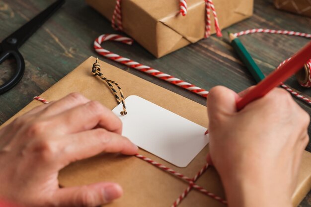 Foto mulher escrevendo etiqueta de presente e anexar ao presente de natal na mesa de madeira