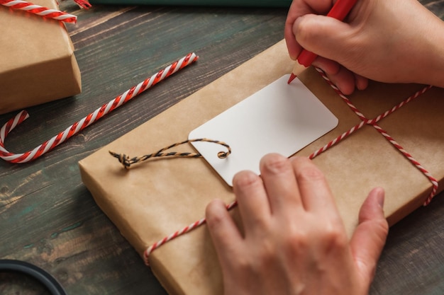 mulher escrevendo etiqueta de presente e anexar ao presente de Natal na mesa de madeira