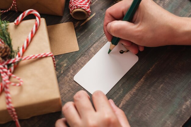 mulher escrevendo etiqueta de presente e anexar ao presente de Natal na mesa de madeira