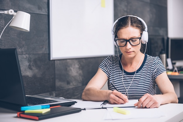 Mulher escrevendo notas e ouvindo música no escritório