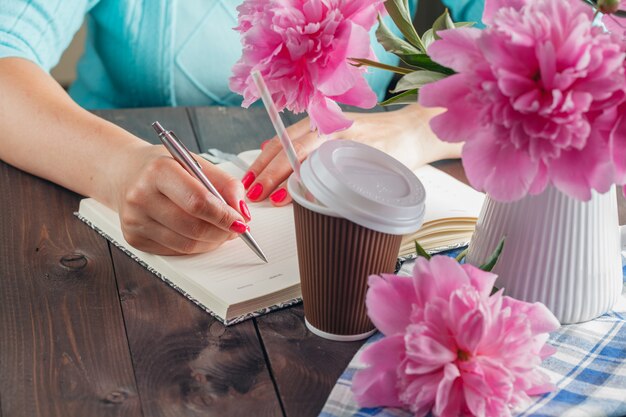 Mulher escrever no caderno, flores na mesa