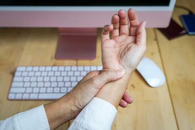 Mulher esfregando a dor no pulso de usar o mouse do computador