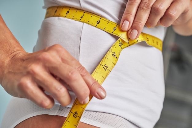 Foto mulher esguia em lingerie branca medindo a cintura