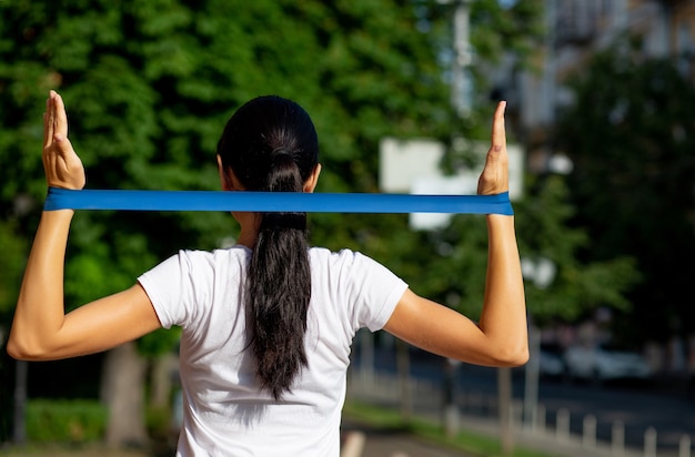 Mulher esguia fazendo exercícios para as mãos com faixa elástica de resistência no parque