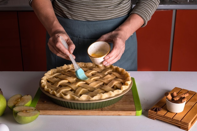 Mulher espalhando ovos na tarte de maçã crua com um pincel de cozinha em um prato de padaria pronto para ser colocado no forno preparação de torta de Ação de Graças padaria de outono doces de clima crocante Receita