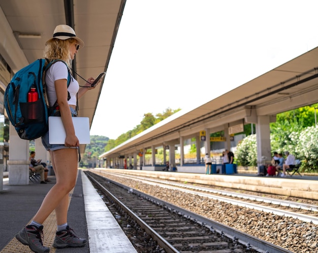 Mulher espera trem na estação enquanto trabalha em viagens nômades digitais por telefone, conceito de transporte