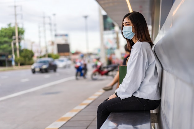 Mulher esperando ônibus no ponto de ônibus na rua da cidade e vestindo máscara protetora para coronavírus
