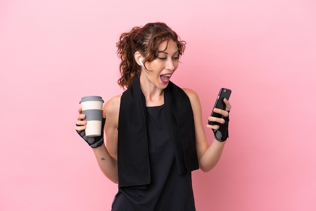 Mulher esporte esporte com toalha isolada em um fundo rosa segurando café para levar e um celular