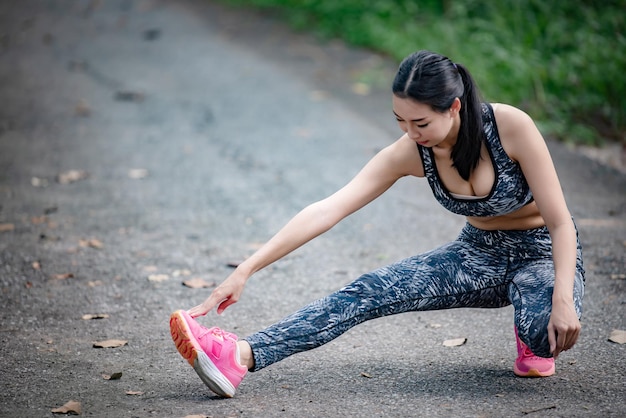 Mulher esportiva asiática esticando o corpo respirando ar fresco no parquePessoas da TailândiaFitness e conceito de exercícioCorrida no parqueCorpo de aquecimento