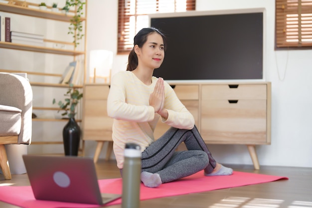 Mulher esportiva assistindo treinamento de ioga on-line e fazendo ioga com pose de namaste e exercício de torção