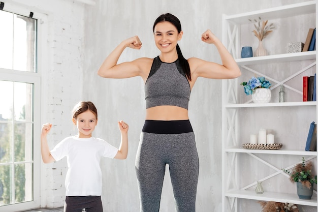 Mulher esportiva atraente e seu filho agradável juntos enquanto mostra os músculos