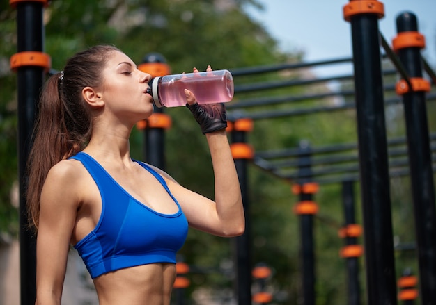 Mulher esportiva bebendo água de vitamina no ginásio de rua