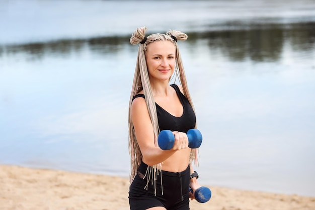 Mulher esportiva caucasiana atraente se exercitando com halteres na praia no verão