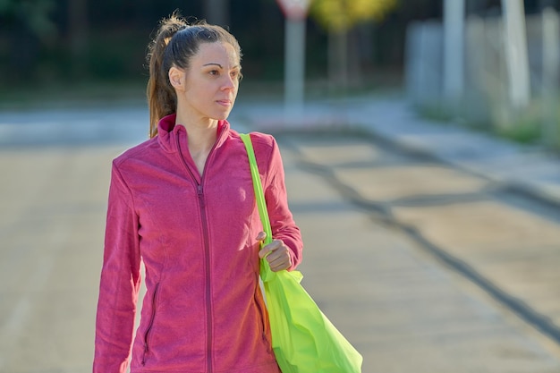 Mulher esportiva com moletom rosa e bolsa amarela andando com espaço de cópia