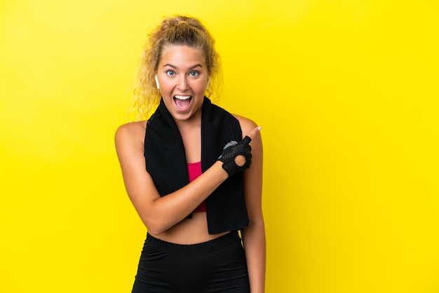 Mulher esportiva com toalha isolada em fundo amarelo surpreso e apontando o lado