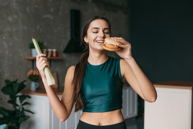 Mulher esportiva escolhendo entre hambúrguer e vegetais na comida lixo da cozinha