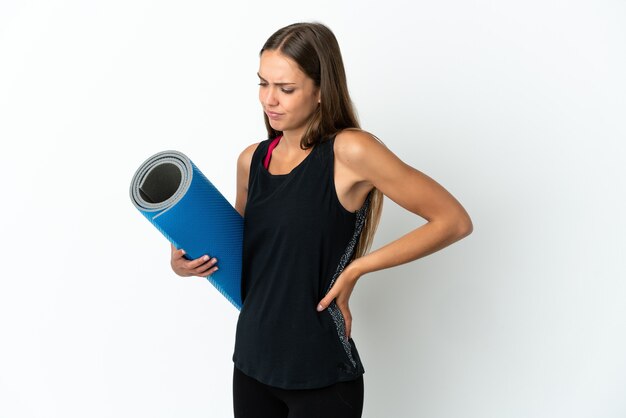 Mulher esportiva indo para aulas de ioga segurando um tapete sobre um fundo branco isolado, sofrendo de dor nas costas por ter feito um esforço