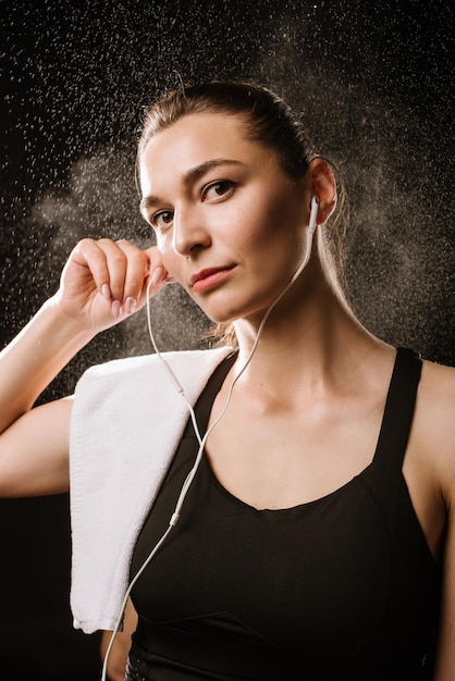 Mulher esportiva magra com fones de ouvido no fundo preto do estúdio