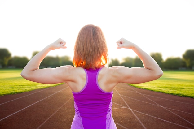 Mulher esportiva na pista se aquecendo antes de correrMulher flexionando seu bíceps