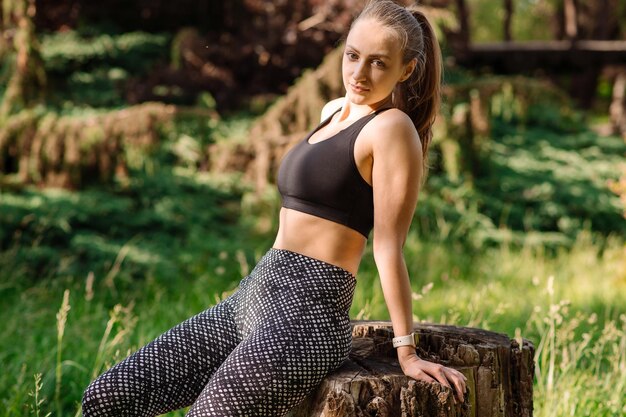 Mulher esportiva relaxando em um tronco de árvore após o treino no parque