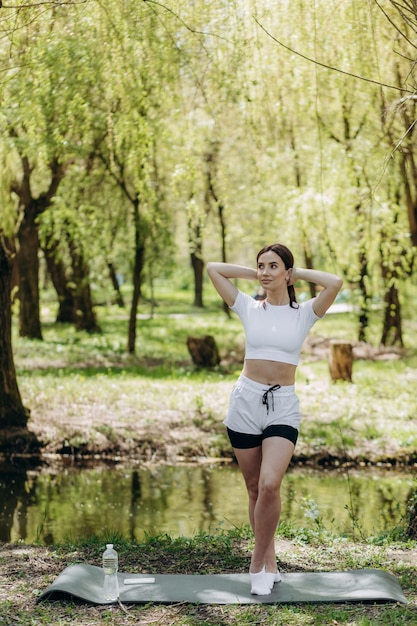 Mulher esportiva segurando nas mãos o tapete de ioga shaker e caminhando para treinar no parque Belo modelo de fitness esportivo durante o treino ao ar livre