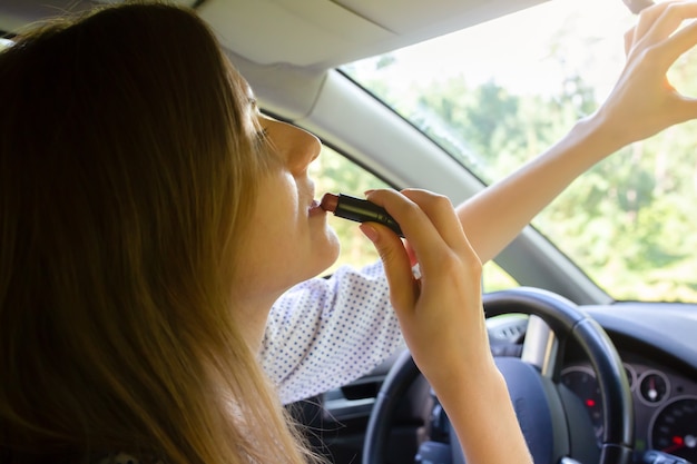 Mulher está aplicando maquiagem no carro. menina com batom ao volante. situação perigosa na estrada. possibilidade de acidente.