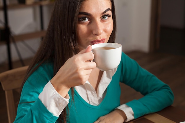 Mulher está bebendo uma xícara branca de café na mesa